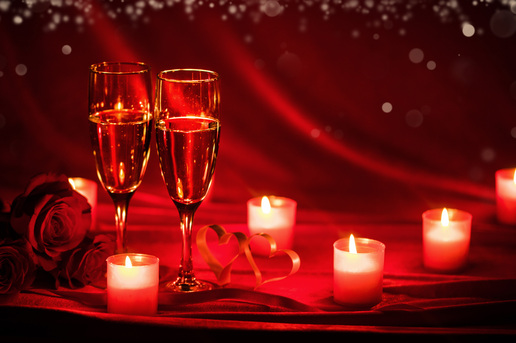 Romantic Valentine’s Day setup with candles, roses, and champagne glasses on a red background.