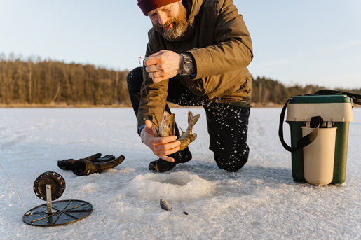 Man ice fishing on a frozen lake in Finland, experiencing traditional Arctic winter activities.